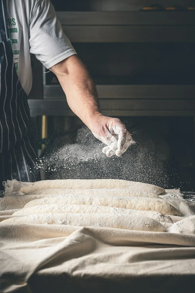 A baker dusting loaves with flour