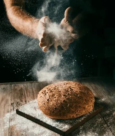 Baker dusting flour over a loaf